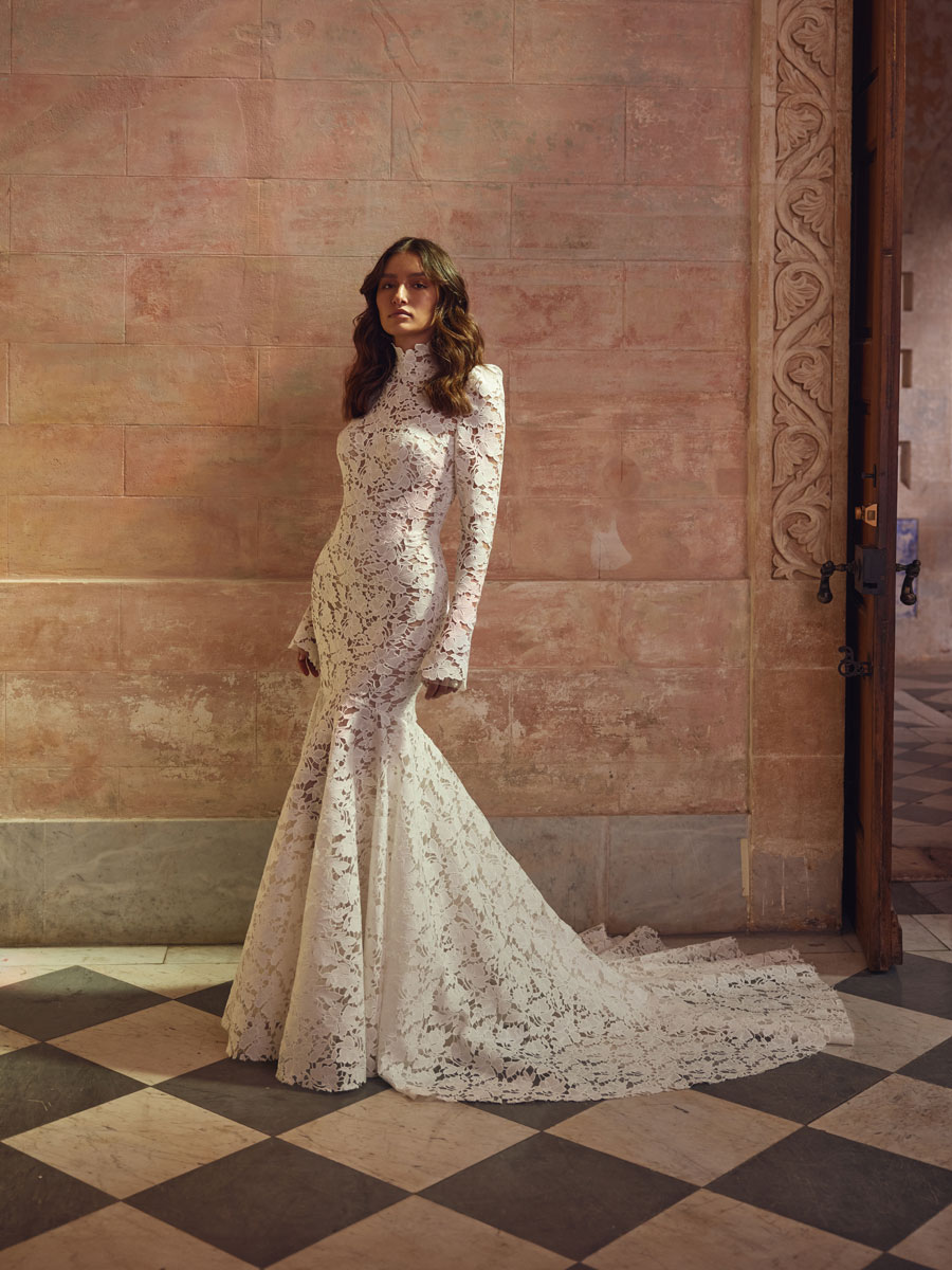 Love Couture Bridal Wedding Dresses. Floral lace wedding dresses worn by a woman near stone columns.