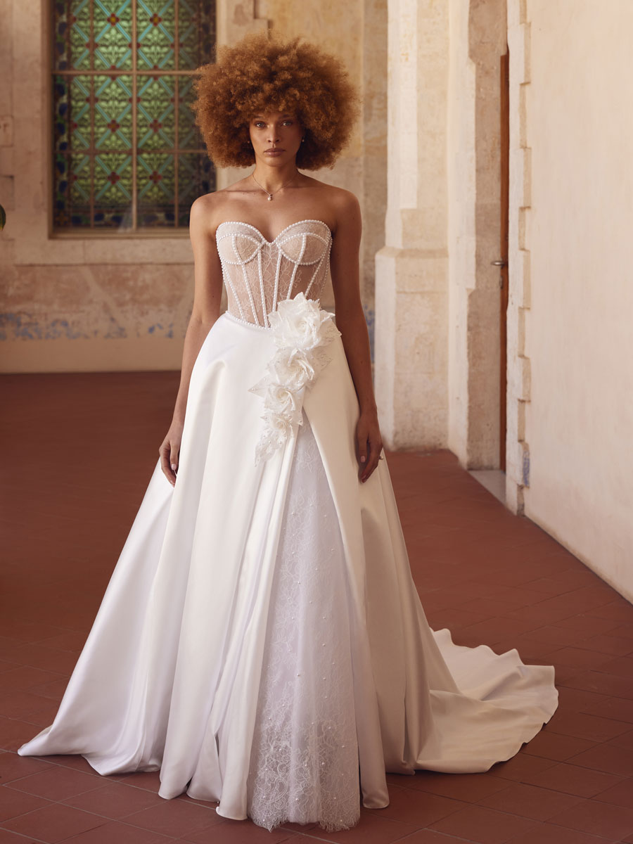 Love Couture Bridal Wedding Dresses. Woman in intricate wedding dresses leaning against old stone ruins.