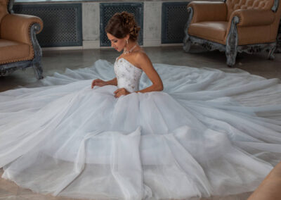 A beautiful bride in a stunning wedding dresses seated gracefully on a white floor, radiating elegance and joy.